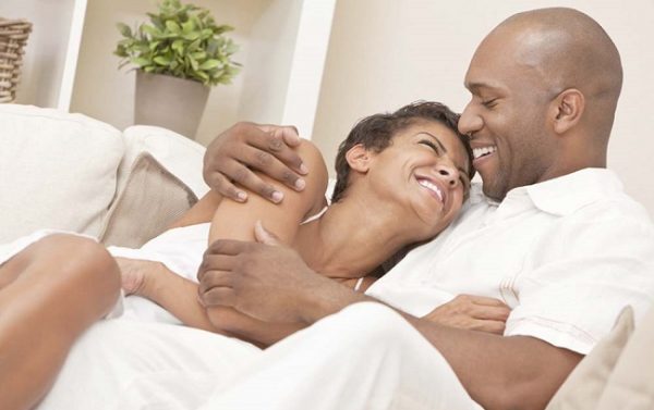 A happy African American man and woman couple in their thirties sitting at home together cuddling & laughing.